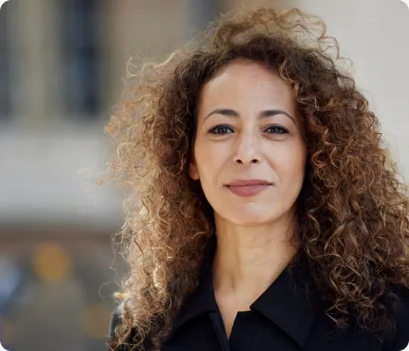 Professional headshot of a person with curly hair wearing a black top against a neutral background.