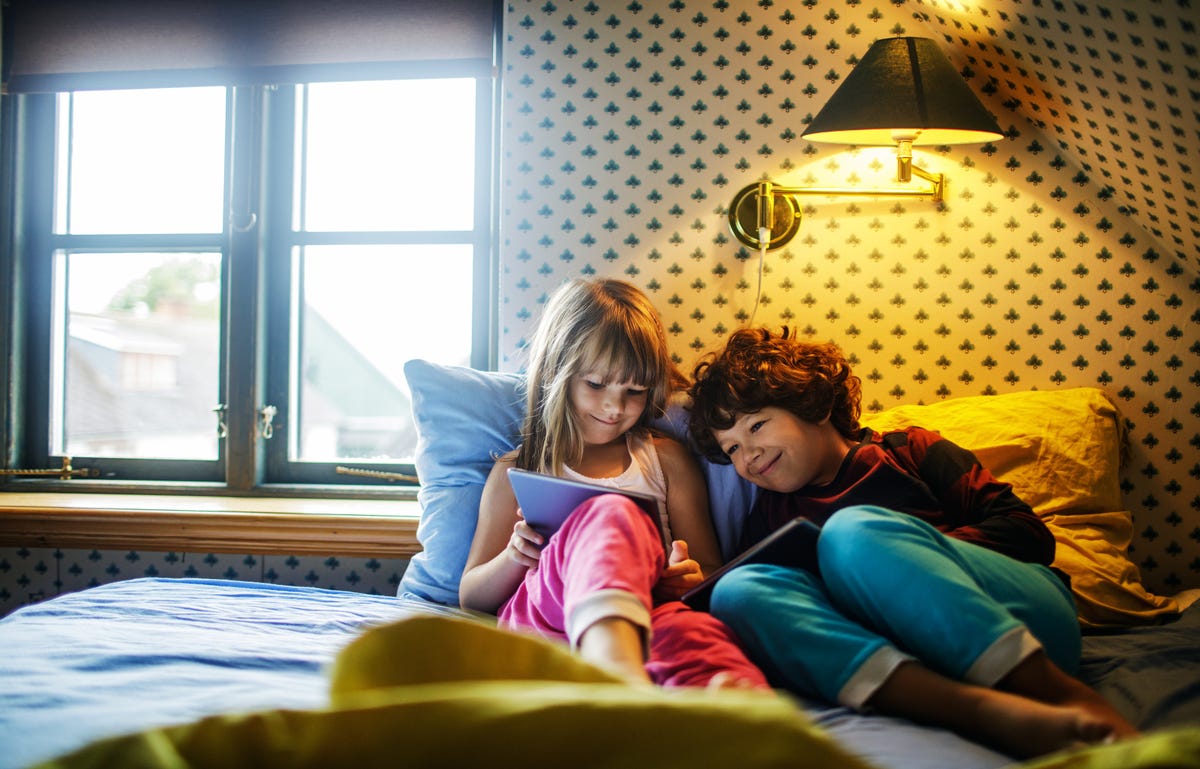 Two children in bed looking at a tablet and taking a German course with Berlitz