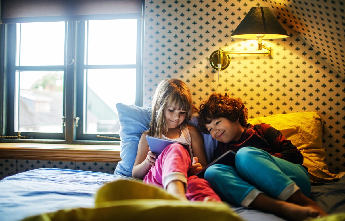Two children in bed looking at a tablet and taking a German course with Berlitz