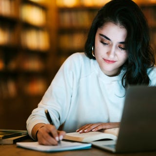 Woman in front of her laptop taking a TOEFL preparation course and taking notes