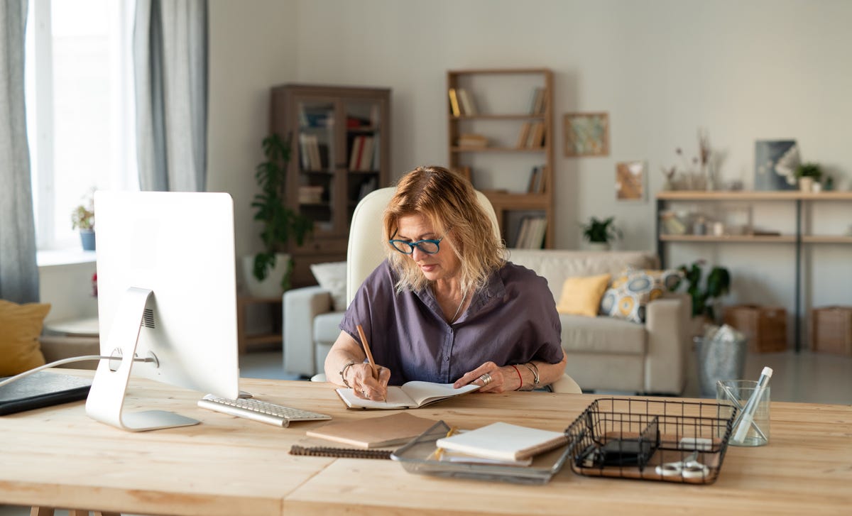 Woman learning a language with Berlitz's self-paced courses on her laptop and making notes in a notebook