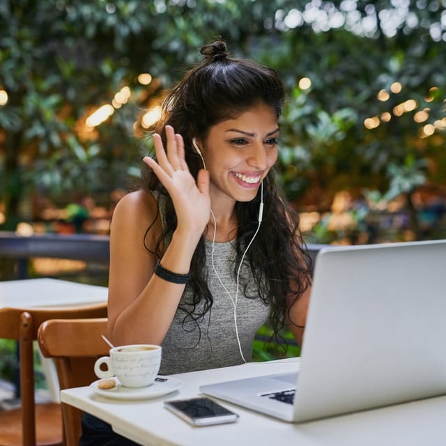 Woman taking an online English class from her laptop and waving at her instructor