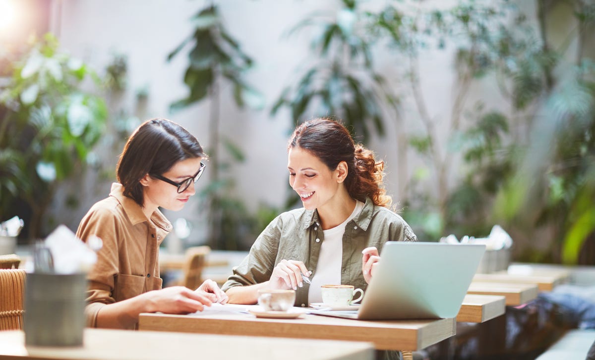 Student and instructor sitting at a desk in front of a laptop and chatting in Spanish