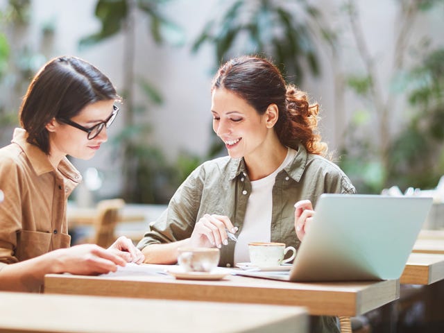 Student and instructor sitting at a desk in front of a laptop and chatting in Spanish