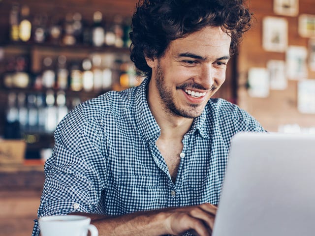 Man with a cup of coffee attending an online group language class with Berlitz Algeria from a coffee shop
