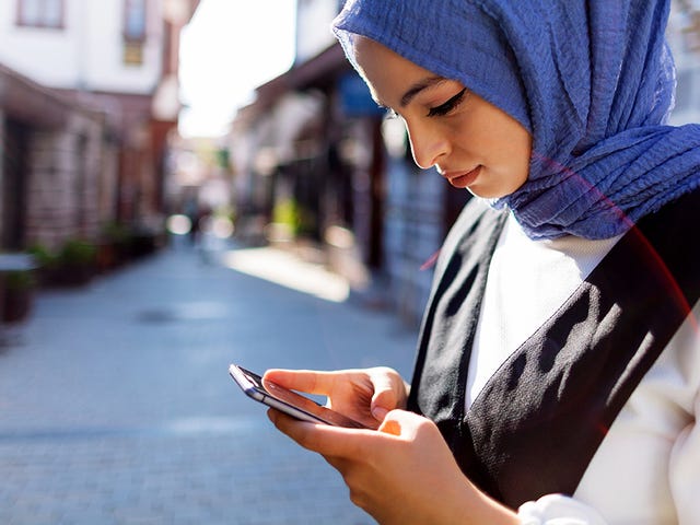 Woman standing on the street and looking up online self-study courses with Berlitz Algeria on her phone
