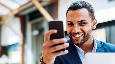 Man in front of a laptop holding his phone and attending an online French course with Berlitz Algeria