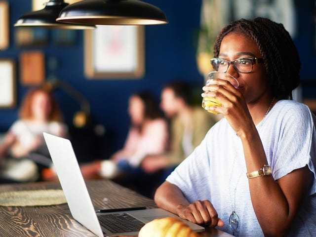 Woman drinking orange juice in a coffee shop and attending an online private class from her laptop
