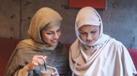 Women in a restaurant drinking coffee and looking up Portuguese classes with Berlitz on a tablet