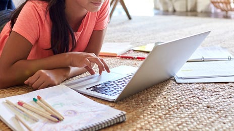 Girl laying on the floor and attending an online language class with Berlitz from her laptop