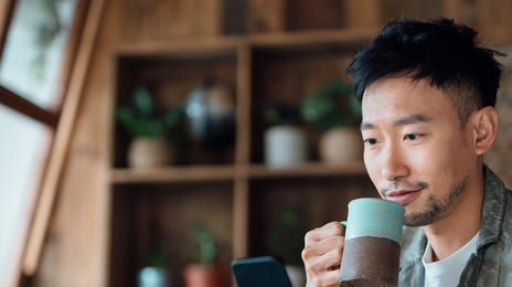Man holding his phone and learning Portuguese online with Berlitz Algeria while drinking coffee from a mug