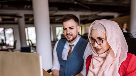 Woman in front of a computer preparing for her TOEFL exam with her instructor sitting next to her