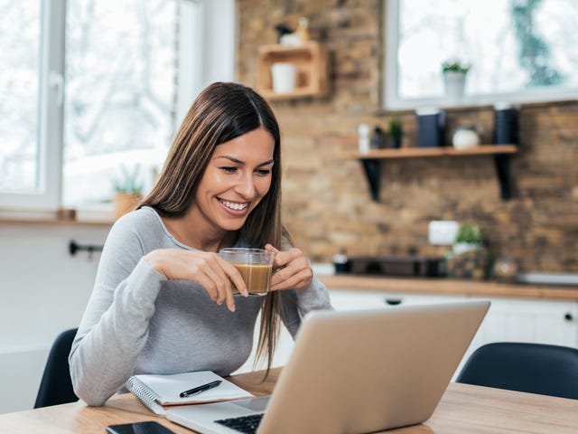 Woman in front of a computer holding a cup of coffee and taking an online self study language course with Berlitz Algeria
