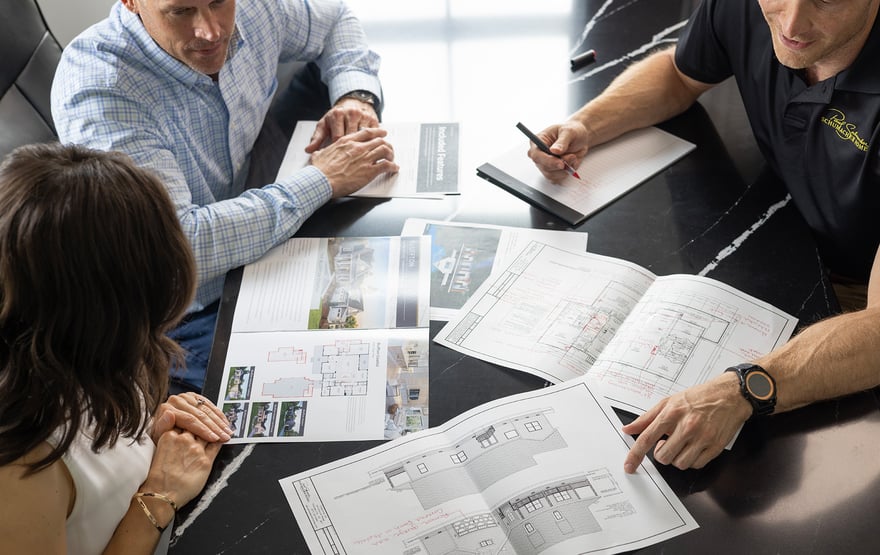 Three people meet at a table, reviewing building plans and included features.