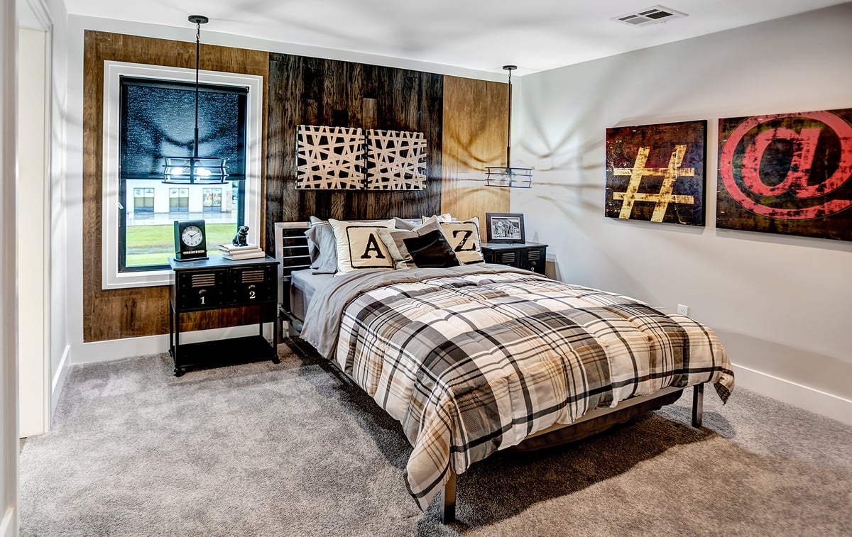 A stylish bedroom features a neutral palette with a plaid comforter. The decor includes geometric art, metal accents, and letter pillows.