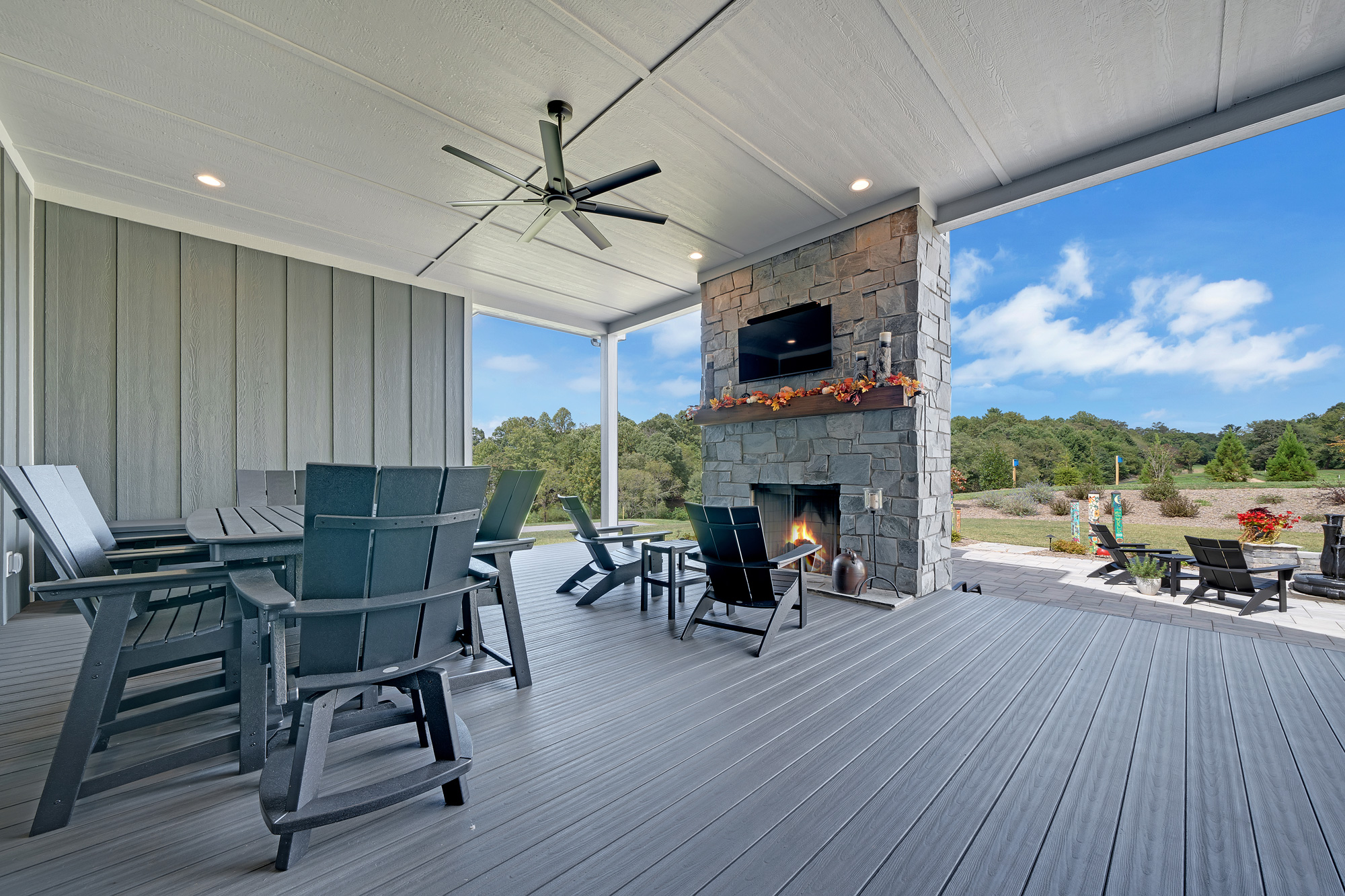 Covered porch extending off the back of a home. There is a large grey fireplace with a wooden mantle.