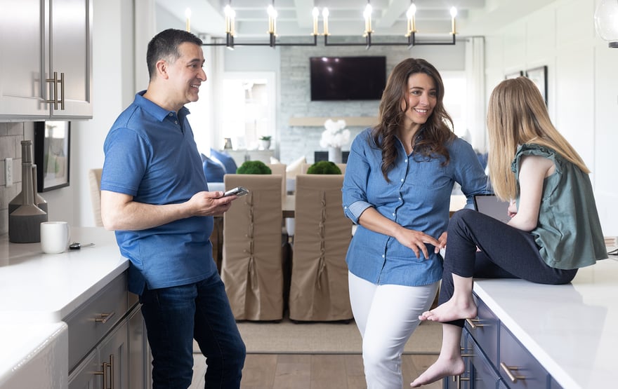 A family gathers in their modern kitchen. A mother and father smile at their child, sitting on the countertop.