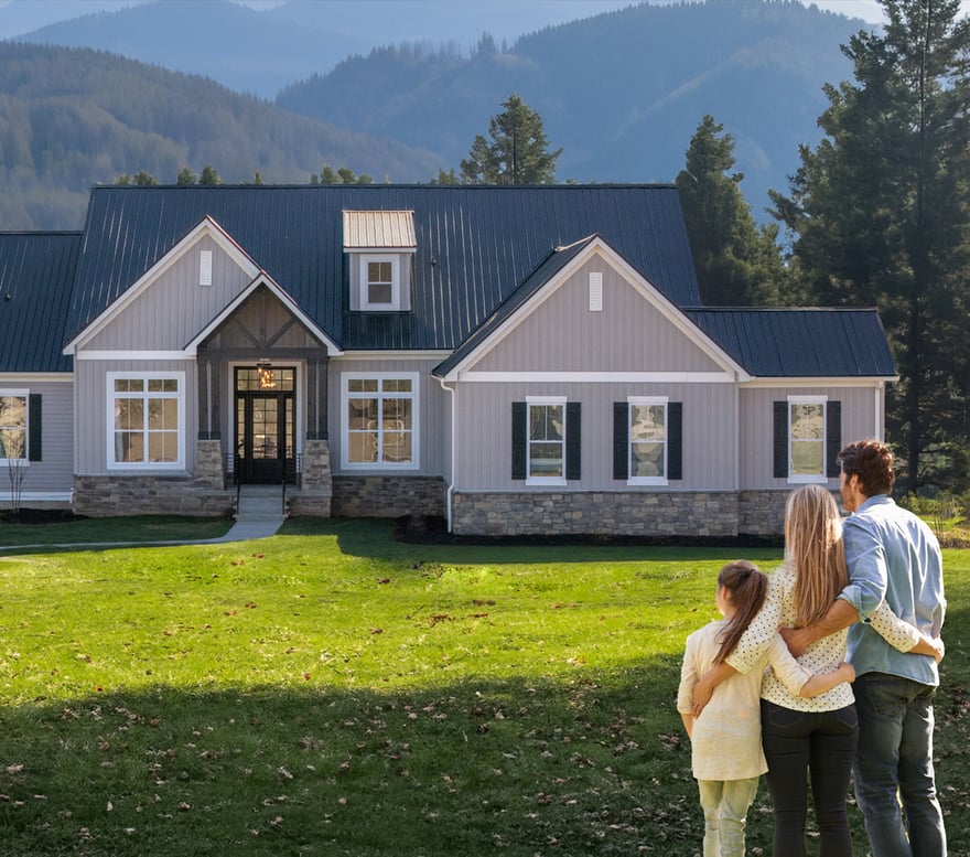 A family stands together looking at their new home set against a mountainous backdrop.