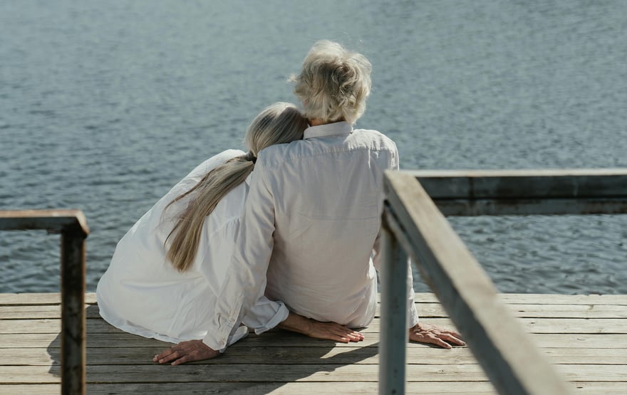 An elderly couple sitting on a dock looking out at the water. 