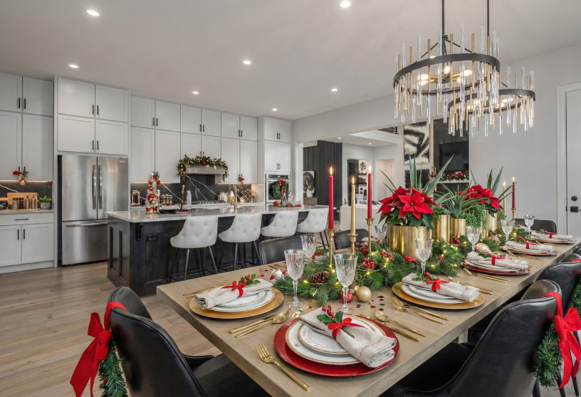 Festive dining room with a table set for Christmas, adorned with red and gold decor, poinsettias, candles, and garlands. Elegant chandelier above.
