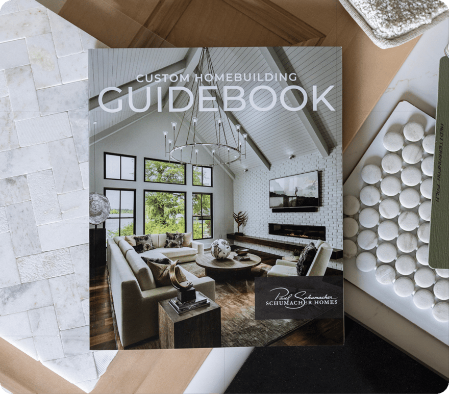 A photo showcasing Schumacher Homes' "Custom Homebuilding Guidebook." The cover features a beautifully designed living room.
