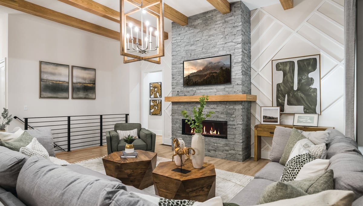 living room wit wooden ceiling beams, and grey brick fireplace with rectangular pendant light.