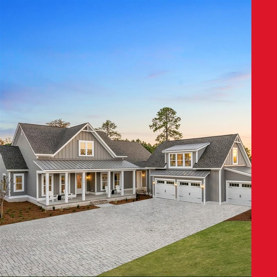 Gray coastal-inspired single-story home with white trim, front porch, three-car garage, and paver driveway at sunset.