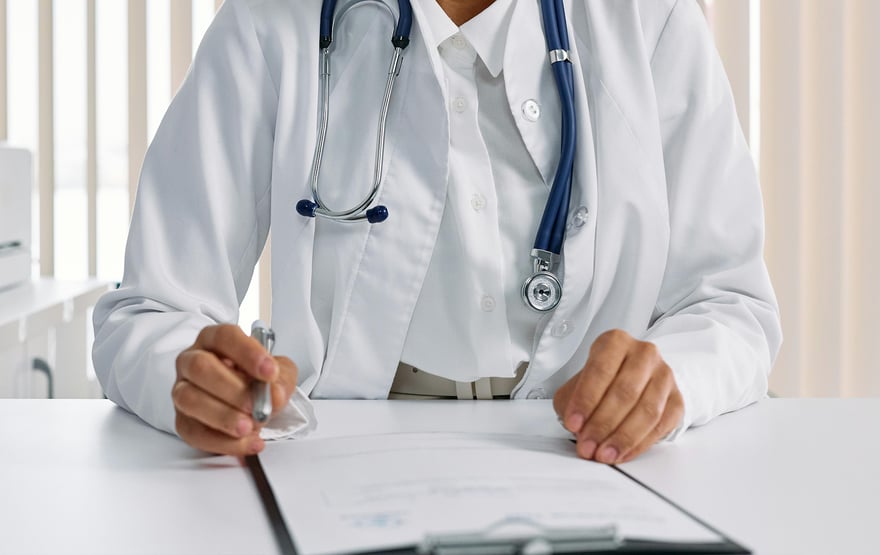 Doctor in a white coat with a stethoscope is writing on a form.