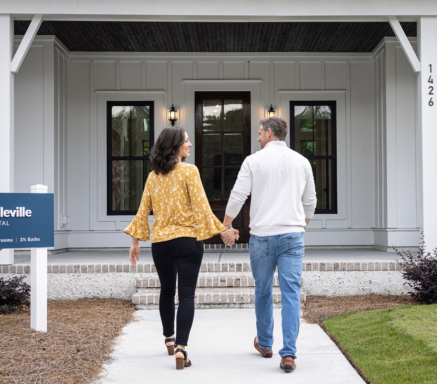 Man and woman holding hands walking up to the front door of a home. 