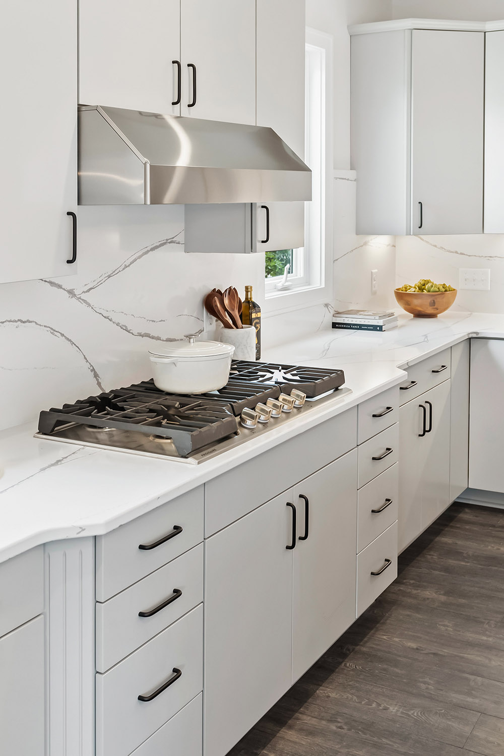 Detail of kitchen range with white Dutch oven on top. There is a white countertop with white tile backsplash behind.