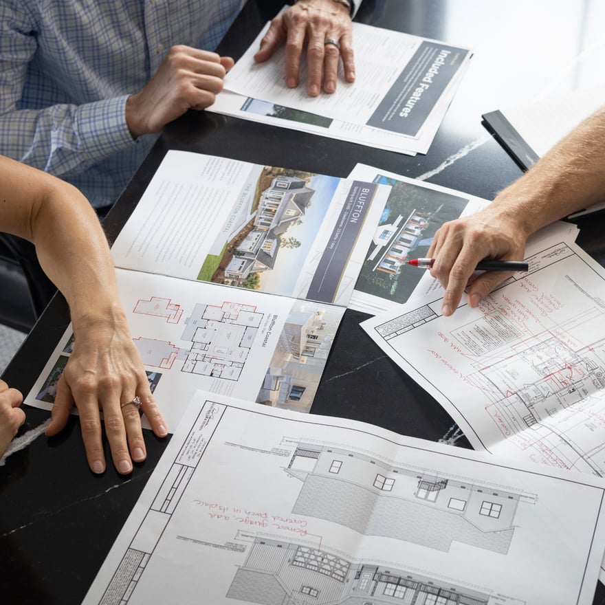 A design team reviews construction plans, with "Included Features" documents present on the table.