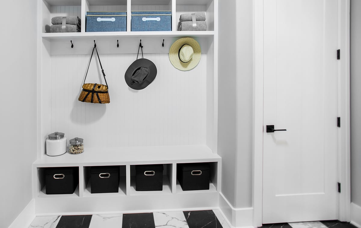 Placeholder
A modern mudroom with built-in storage. The space is organized with baskets, towels, hats, and bags, and features black and white flooring.
