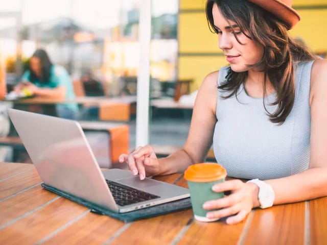 Mujer joven haciendo una prueba de nivel de inglés en su portátil, con café en mano, desde un café moderno junto a Bertliz.