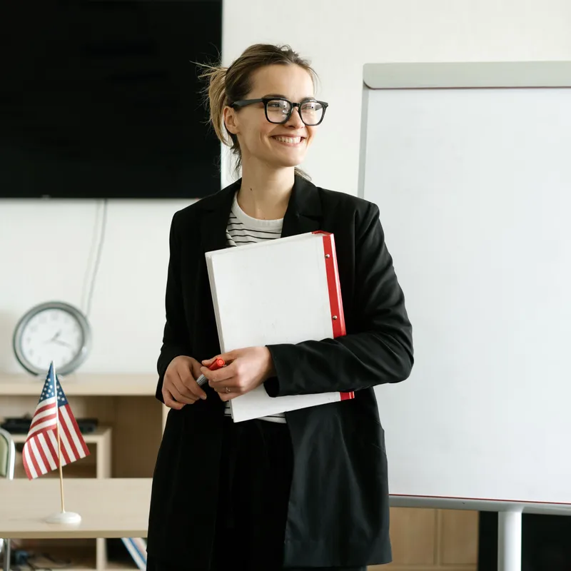 Una maestra sonriendo en un salón de clases para representar una buena profesora de inglés.