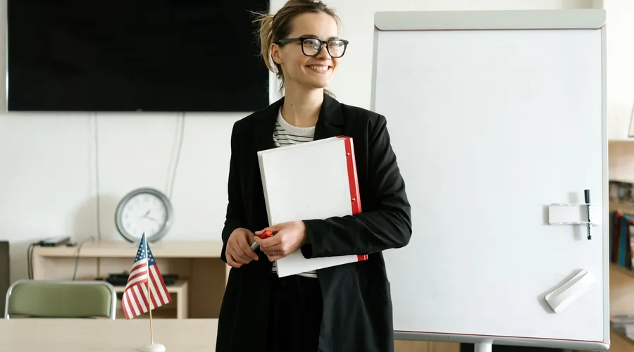 Una maestra sonriendo en un salón de clases para representar una buena profesora de inglés.