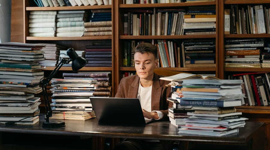 Chico estudiando en su laptop rodeado de libros sobre rutas de aprendizaje.