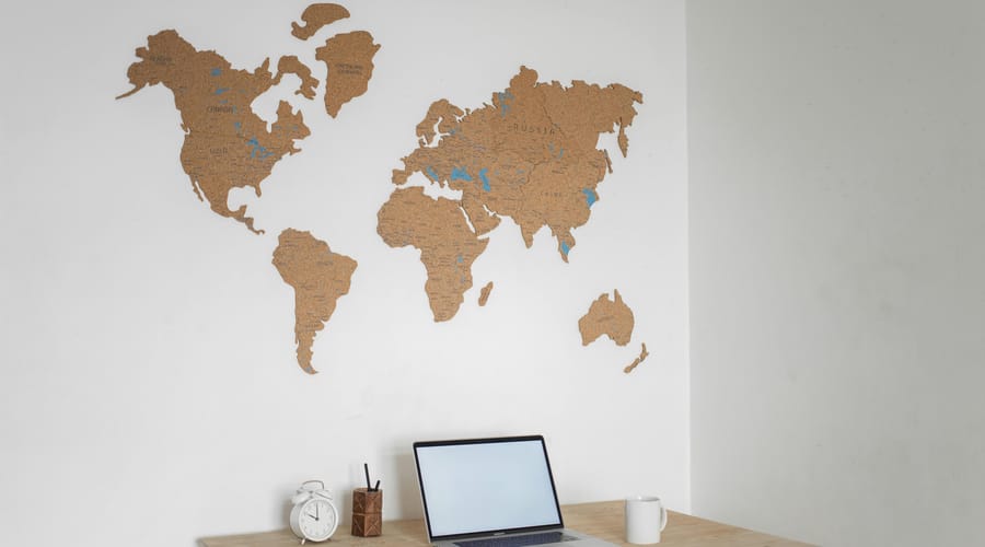 Un escritorio con un mapa del mundo en la pared, un reloj, una taza y una laptop para representar el mercado laboral.