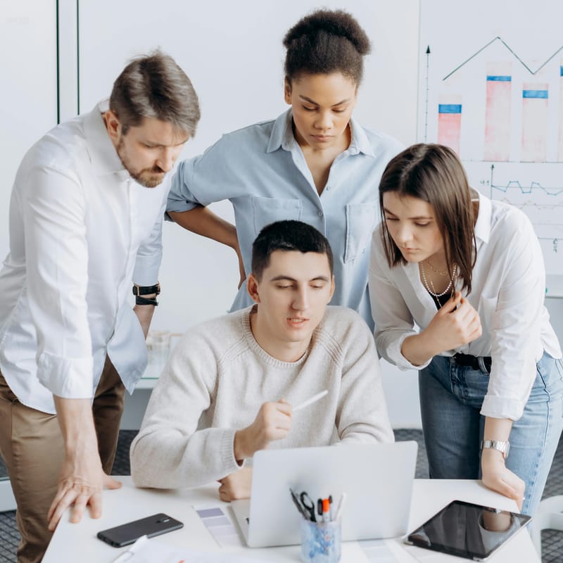 Equipo de trabajo multicultural colaborando frente a una computadora portátil en una reunión laboral, analizando información y gráficos en un entorno corporativo.
