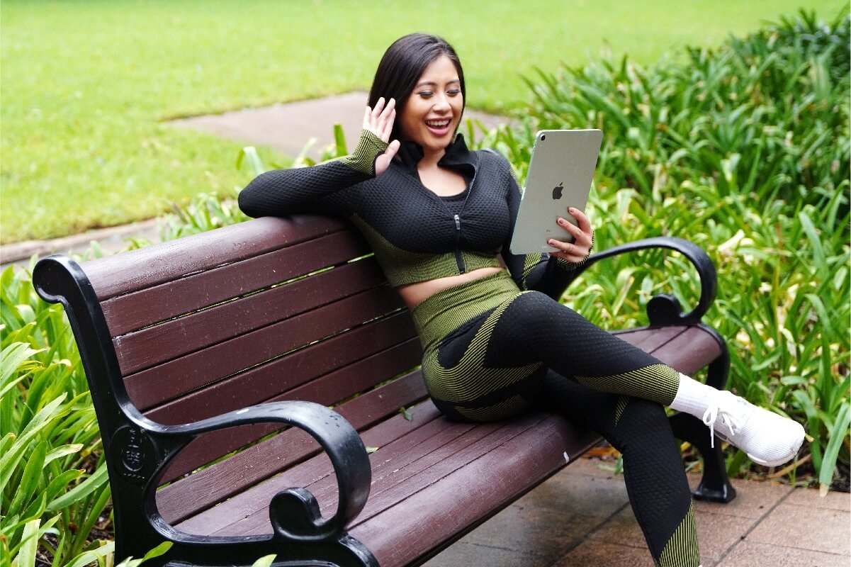 Estudiante sonriente en una clase virtual de idiomas con Berlitz desde un parque, combinando su estilo de vida activo con el aprendizaje flexible.