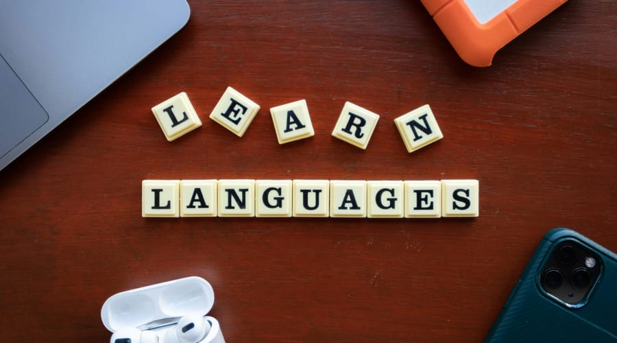 Fichas con la frase “Learn Languages” sobre un escritorio, junto a audífonos, un celular y una laptop, simbolizando el aprendizaje de idiomas.
