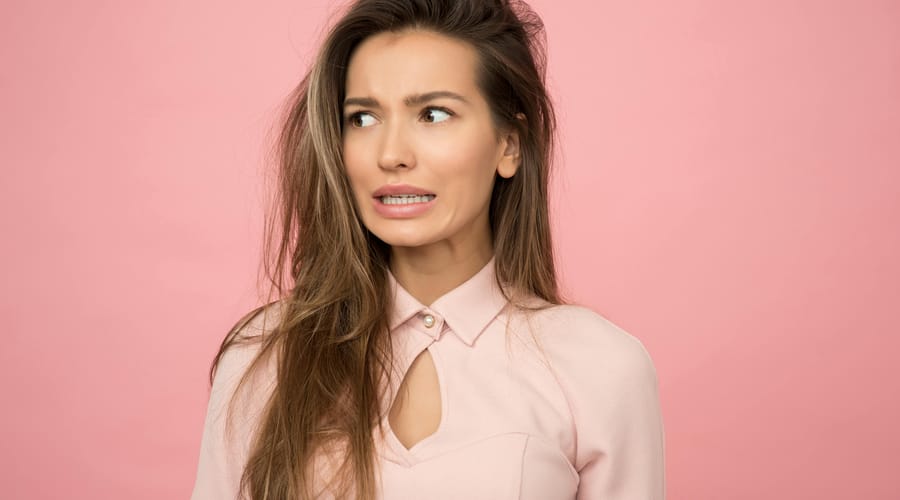 Mujer con cara de preocupación por olvidar su idioma natal. Fondo rosa.