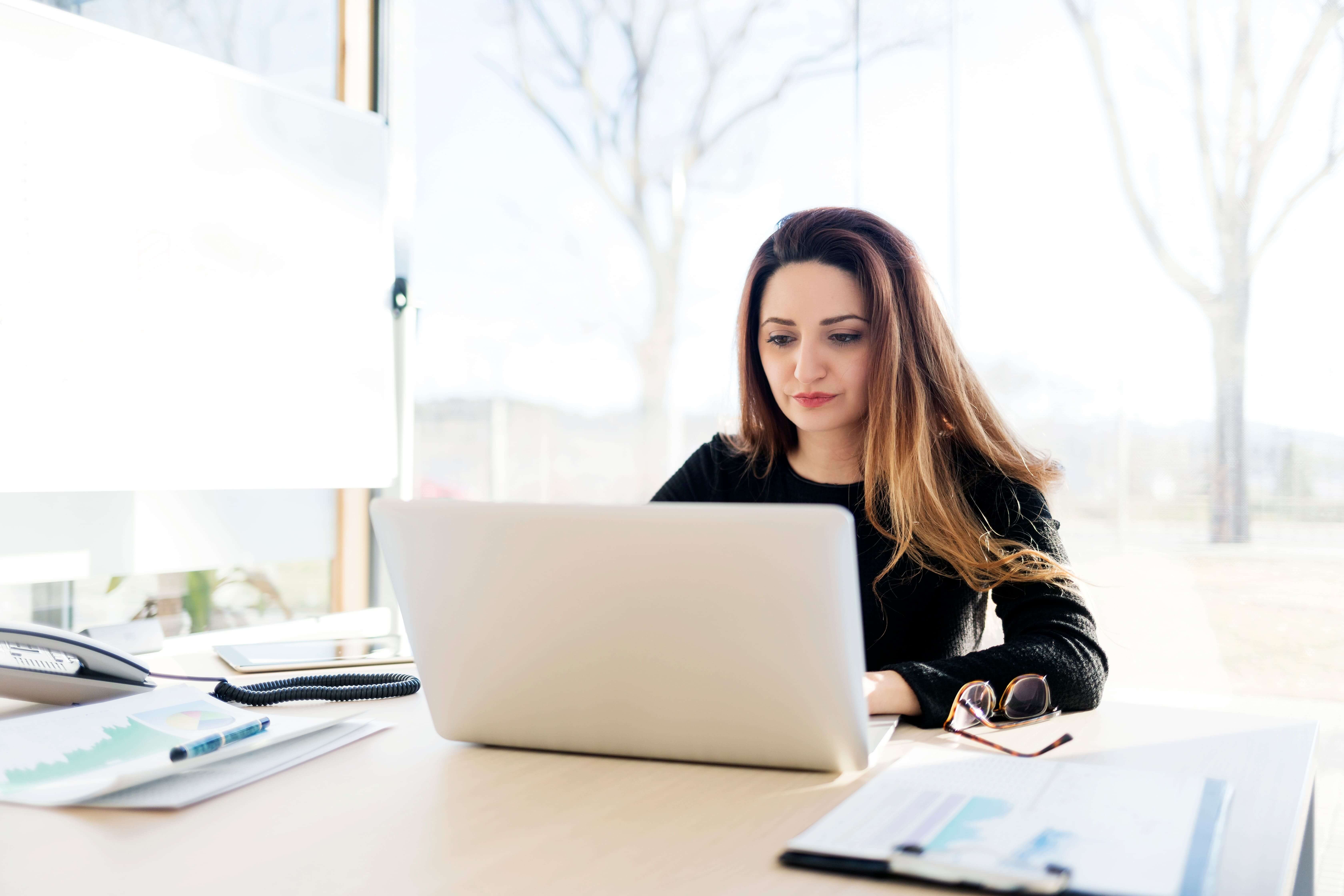 Profesional enfocada en su desarrollo de carrera, realizando una prueba de nivel de idiomas en su portátil con Berlitz desde una oficina moderna.