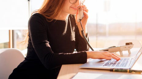 Mujer joven recomendando clases de italiano con Berlitz por teléfono mientras trabaja en su laptop.