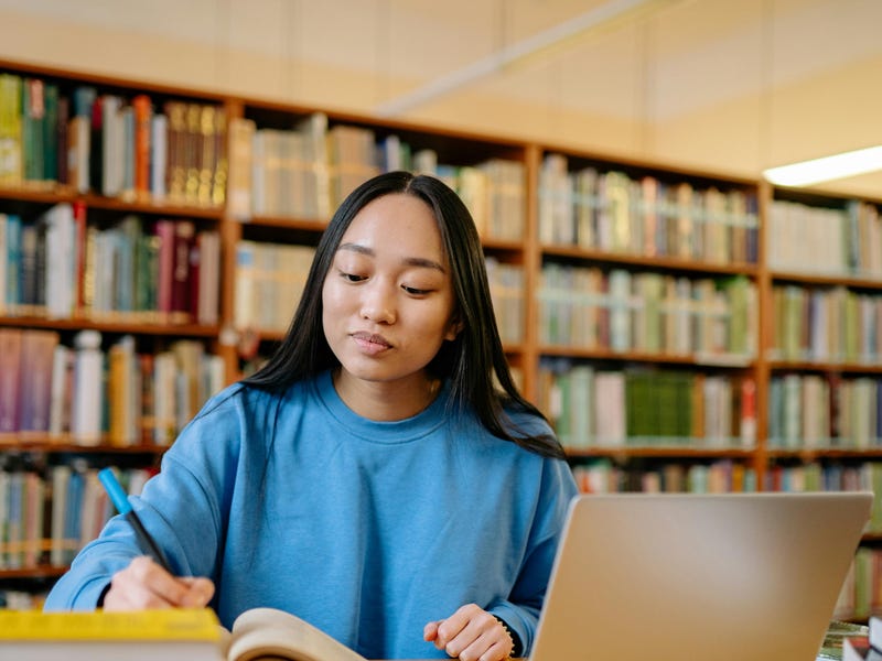 Chica estudiando portugués online en una biblioteca.