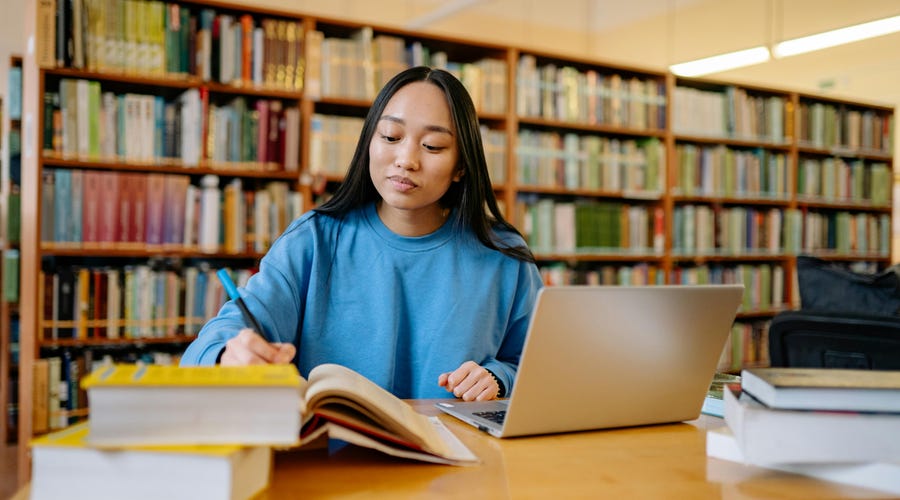 Chica estudiando portugués online en una biblioteca.