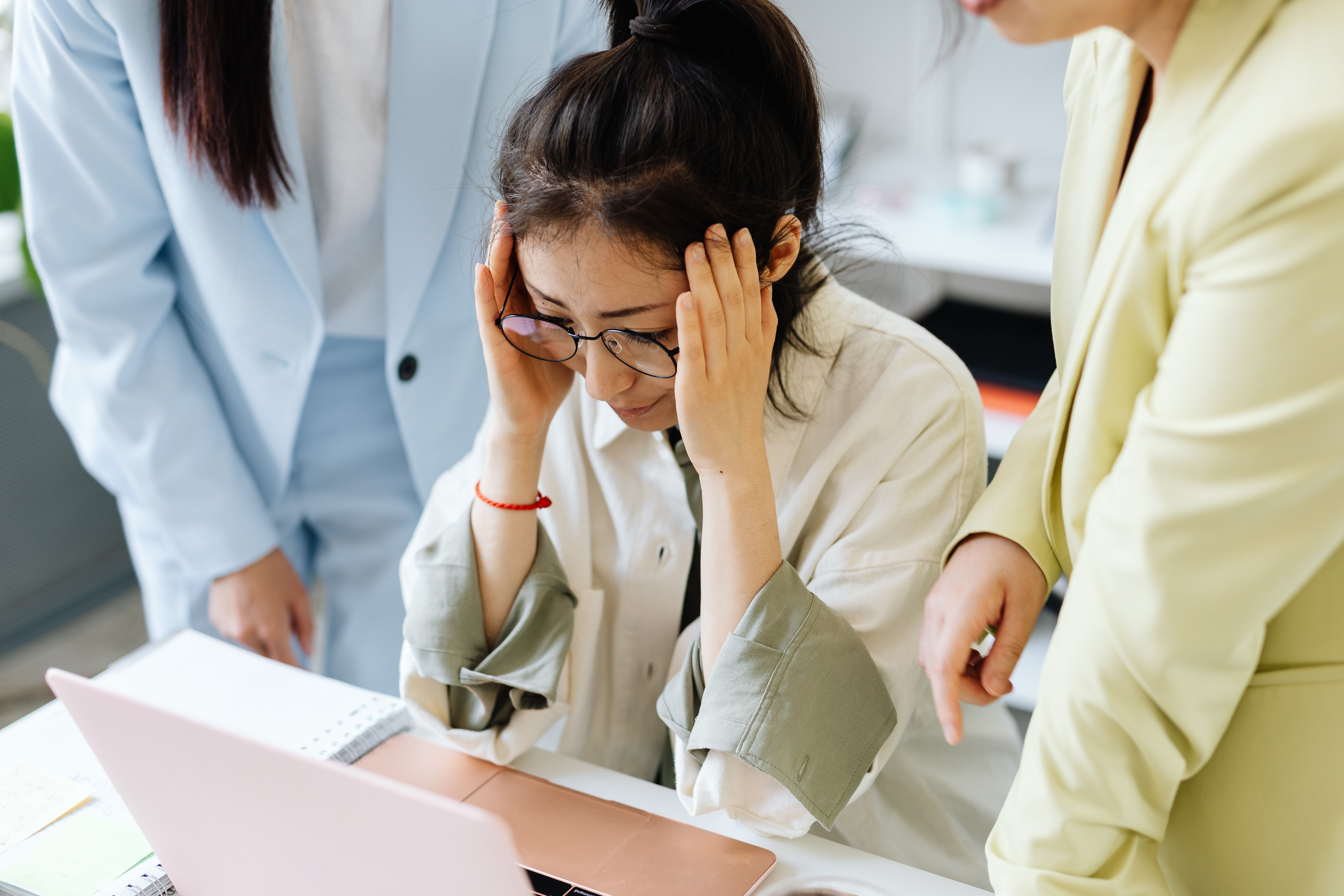 Mujer con dolor de cabeza en el trabajo por sentir presión social por no hablar inglés.