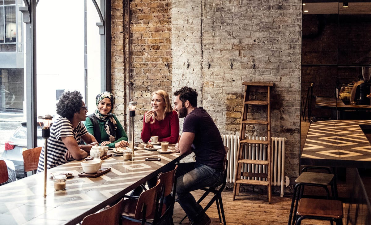 Grupo de jóvenes de diversas culturas compartiendo en una cafetería, símbolo de inclusión, conexión global y el poder del aprendizaje de idiomas con Berlitz.