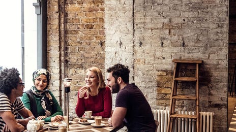 Grupo de jóvenes de diversas culturas compartiendo en una cafetería, símbolo de inclusión, conexión global y el poder del aprendizaje de idiomas con Berlitz.