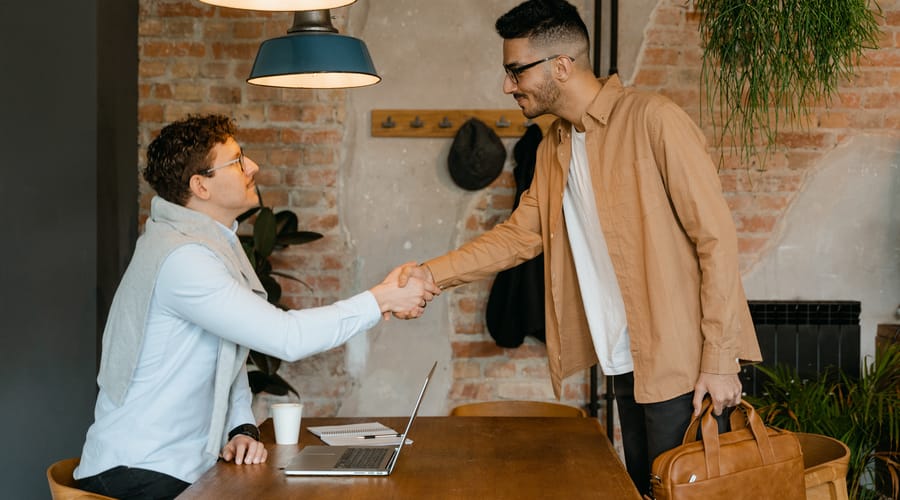 Dos personas saludándose con un apretón de manos para representar el saludo en inglés.