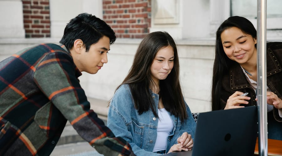 Tres estudiantes jóvenes colaboran frente a una laptop en un entorno universitario para estudiar temas de inglés c1.
